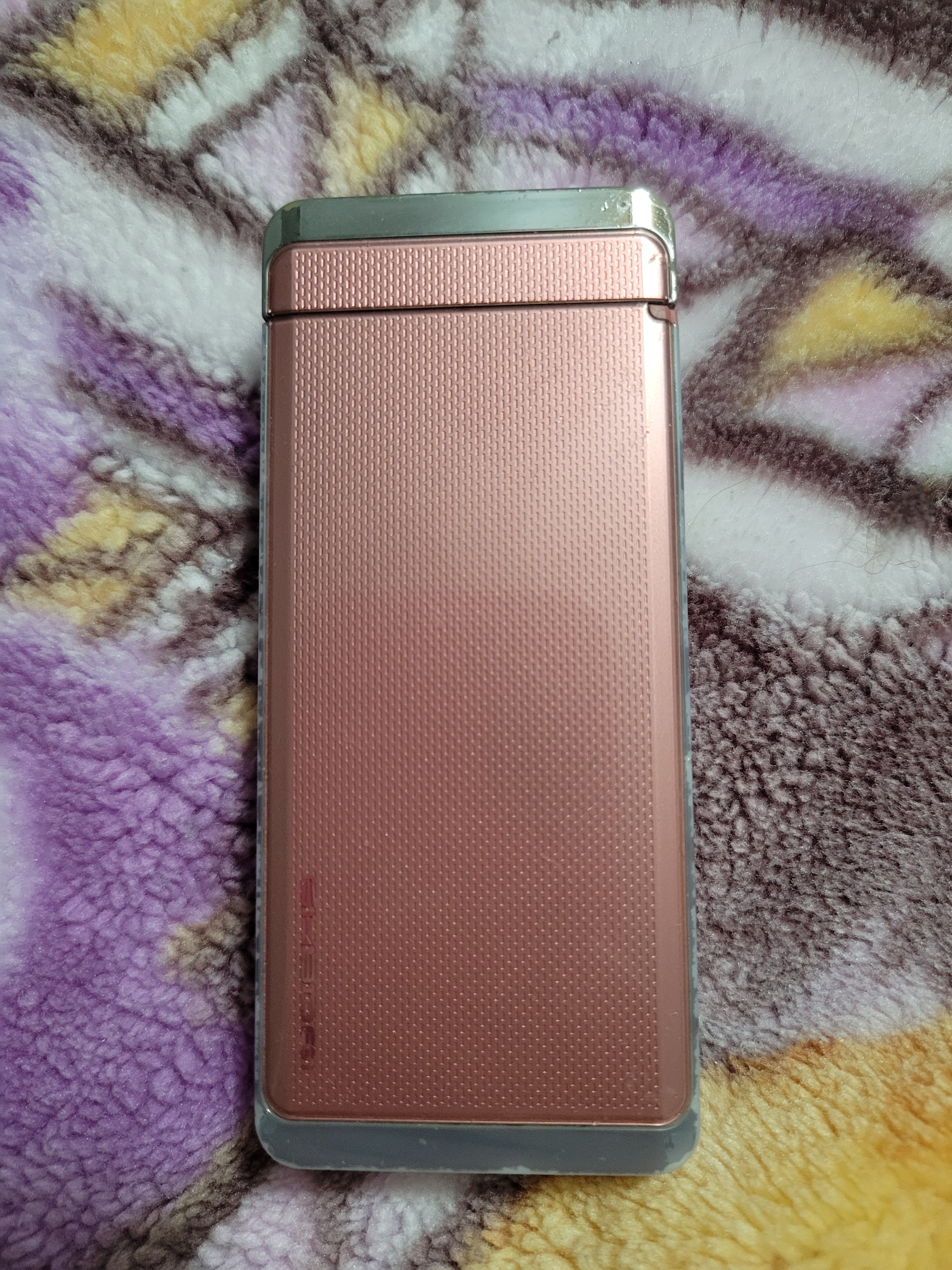 Top of closed pink Japanese flip phone on top of a fuzzy blanket